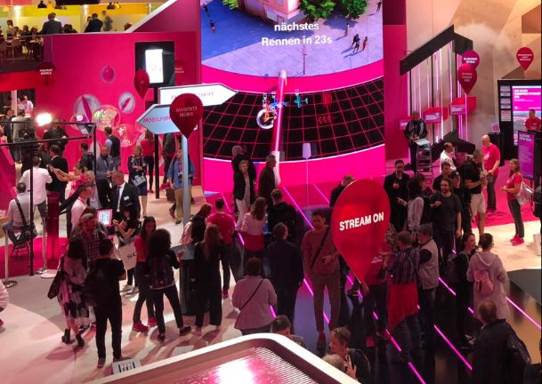 A photo of many visitors at the Telekom booth playing a game on a big screen