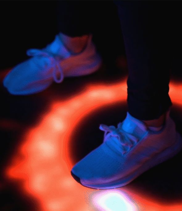 A photo of two feet in white sneakers standing on a balance board which has a colorful animated Interface.