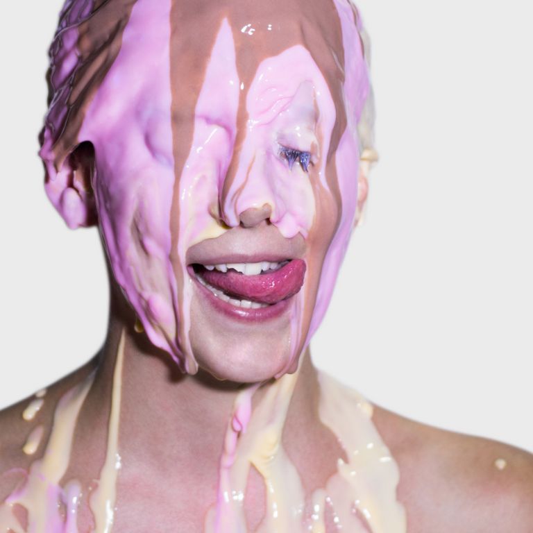 A woman being showered with colorful custard. She is trying to lick it off her face.